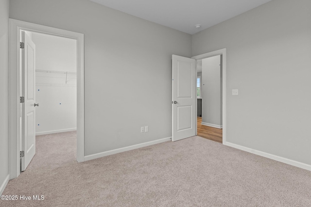 unfurnished bedroom with a spacious closet, a closet, and light colored carpet