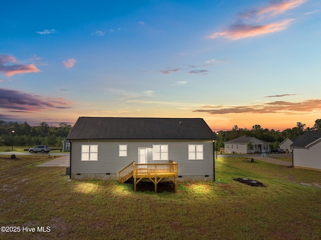 back house at dusk with a wooden deck and a lawn