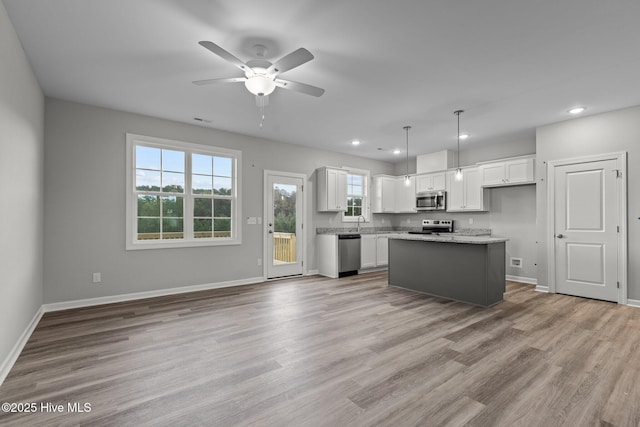 kitchen with a kitchen island, white cabinets, hanging light fixtures, and appliances with stainless steel finishes