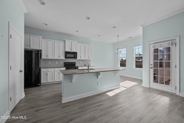 kitchen featuring a kitchen breakfast bar, sink, black appliances, a center island with sink, and white cabinets