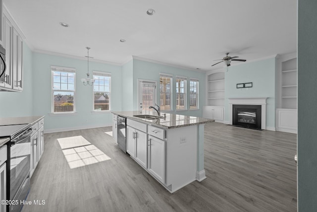 kitchen with built in shelves, white cabinetry, hanging light fixtures, black / electric stove, and a center island with sink