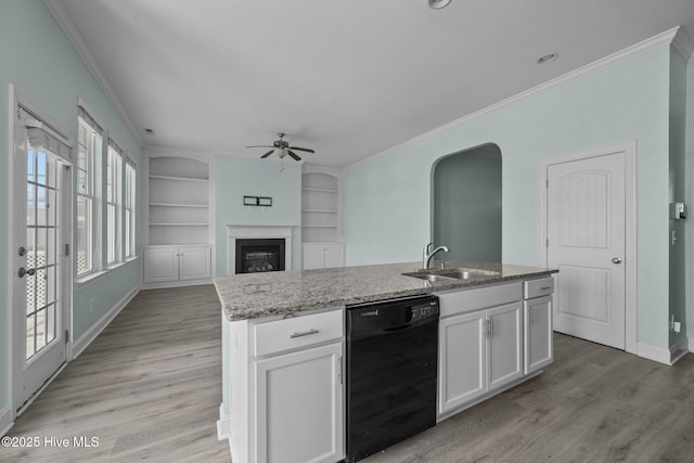 kitchen with sink, built in features, black dishwasher, white cabinetry, and an island with sink