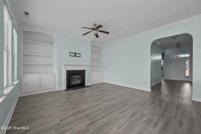 unfurnished living room featuring hardwood / wood-style floors, built in shelves, ceiling fan, and crown molding