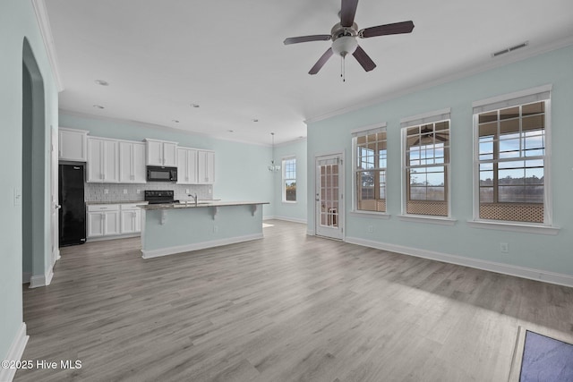 kitchen featuring tasteful backsplash, an island with sink, a breakfast bar, white cabinets, and black appliances