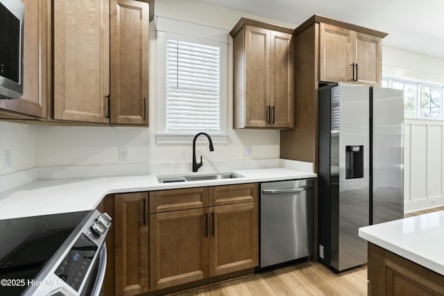 kitchen with light stone counters, sink, light wood-type flooring, and appliances with stainless steel finishes