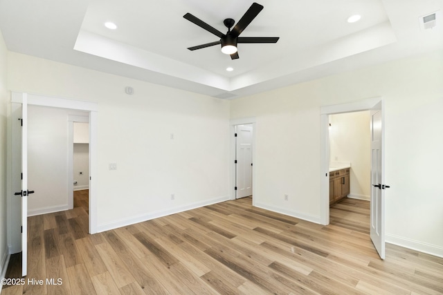 unfurnished bedroom featuring a tray ceiling, connected bathroom, ceiling fan, and light wood-type flooring