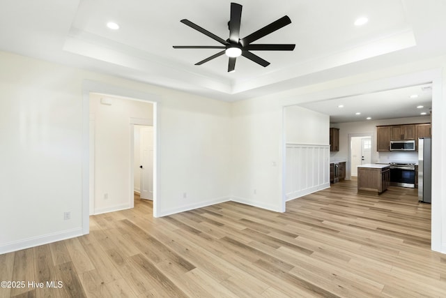 unfurnished living room featuring a raised ceiling, ceiling fan, and light hardwood / wood-style floors