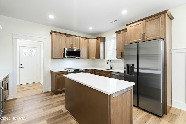 kitchen with sink, light hardwood / wood-style flooring, a kitchen island, and appliances with stainless steel finishes