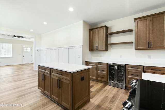 kitchen with stove, light wood-type flooring, beverage cooler, ceiling fan, and a kitchen island