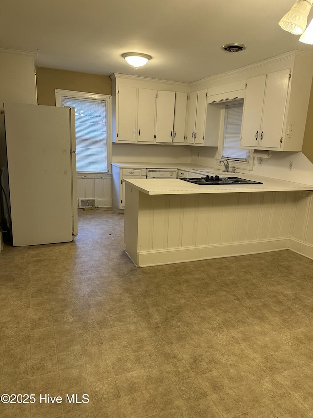 kitchen featuring kitchen peninsula, a kitchen bar, white refrigerator, and white cabinets