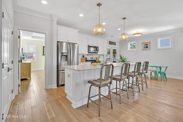 kitchen featuring decorative light fixtures, white cabinetry, stainless steel appliances, an island with sink, and light stone counters