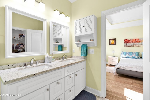 ensuite bathroom featuring double vanity, wood finished floors, baseboards, and a sink