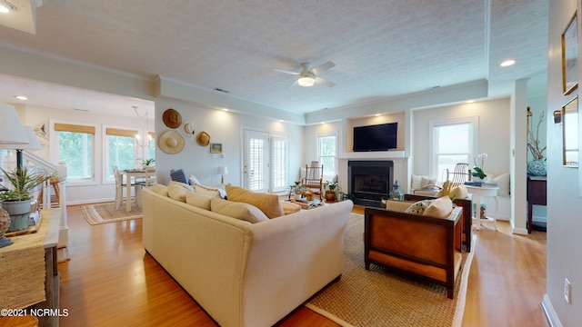 living room featuring ceiling fan, light hardwood / wood-style floors, a textured ceiling, and a wealth of natural light