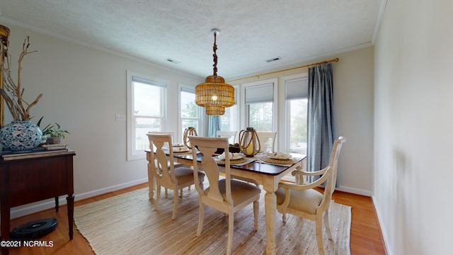 dining room featuring a textured ceiling, light hardwood / wood-style floors, and ornamental molding