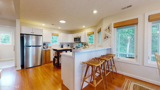 kitchen featuring kitchen peninsula, light hardwood / wood-style flooring, appliances with stainless steel finishes, a kitchen bar, and white cabinetry