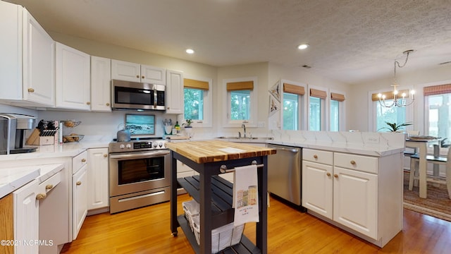 kitchen with white cabinetry, sink, stainless steel appliances, and decorative light fixtures