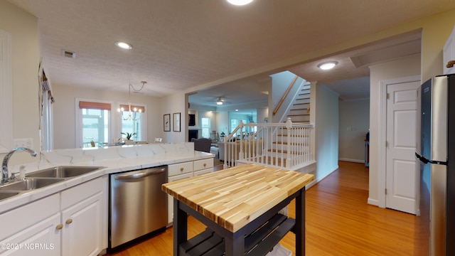 kitchen with appliances with stainless steel finishes, light wood-type flooring, decorative light fixtures, white cabinets, and a chandelier