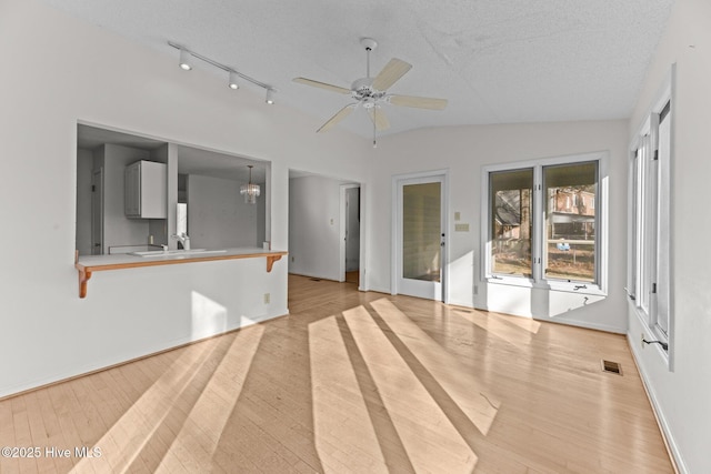 unfurnished living room featuring vaulted ceiling, ceiling fan with notable chandelier, a textured ceiling, and light hardwood / wood-style floors