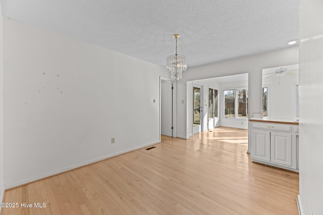 empty room featuring ceiling fan with notable chandelier, a textured ceiling, and light hardwood / wood-style flooring