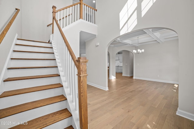 stairway with a high ceiling, an inviting chandelier, coffered ceiling, beamed ceiling, and hardwood / wood-style flooring