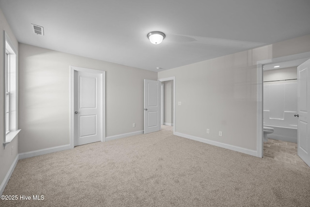 unfurnished bedroom featuring light colored carpet and ensuite bath