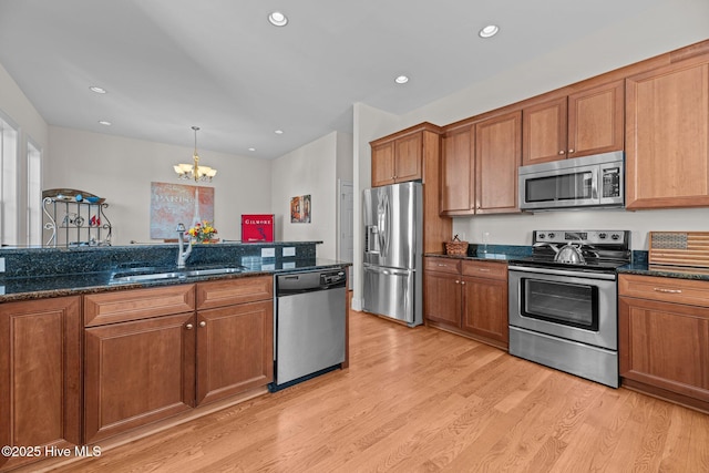 kitchen with sink, light wood-type flooring, stainless steel appliances, dark stone counters, and a chandelier