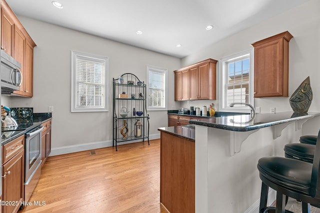 kitchen featuring a kitchen bar, kitchen peninsula, appliances with stainless steel finishes, light wood-type flooring, and dark stone counters