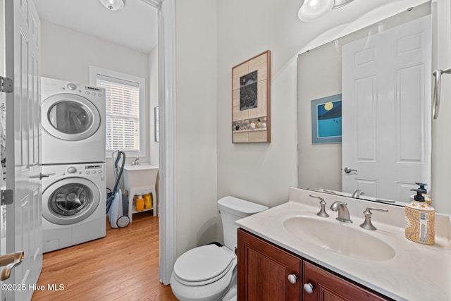 bathroom with hardwood / wood-style floors, stacked washer / drying machine, vanity, and toilet