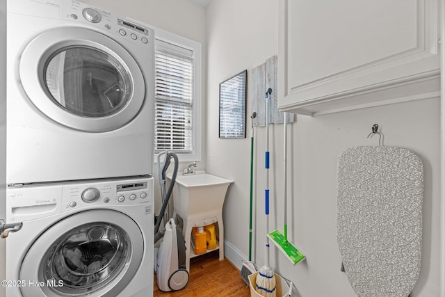 washroom featuring hardwood / wood-style flooring, cabinets, and stacked washer and clothes dryer