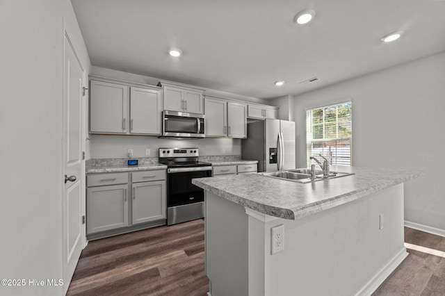 kitchen featuring sink, dark wood-type flooring, stainless steel appliances, gray cabinets, and a kitchen island with sink