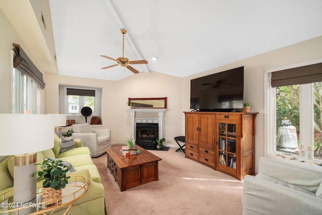 living room featuring vaulted ceiling with beams, light colored carpet, a premium fireplace, and ceiling fan