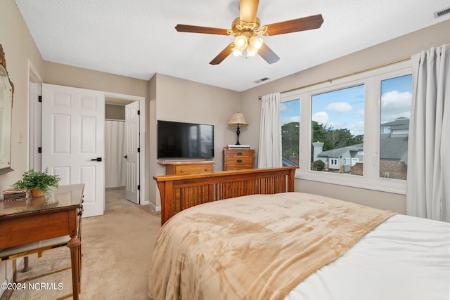 bedroom with ceiling fan, light carpet, and a textured ceiling