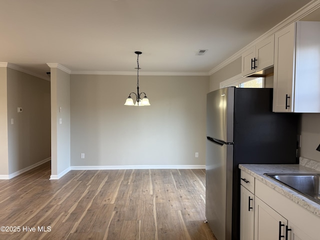 kitchen with stainless steel fridge, light wood-type flooring, crown molding, an inviting chandelier, and white cabinets