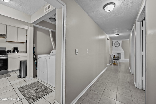 corridor featuring light tile patterned floors, a textured ceiling, and separate washer and dryer