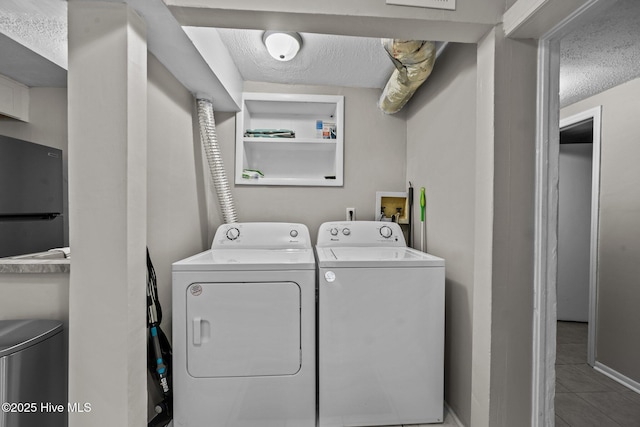 clothes washing area featuring washing machine and dryer, light tile patterned floors, and a textured ceiling