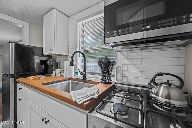 kitchen with sink, stainless steel appliances, a textured ceiling, decorative backsplash, and white cabinets