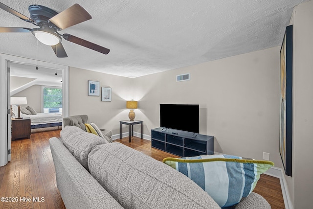 living room with a textured ceiling, ceiling fan, and dark hardwood / wood-style floors