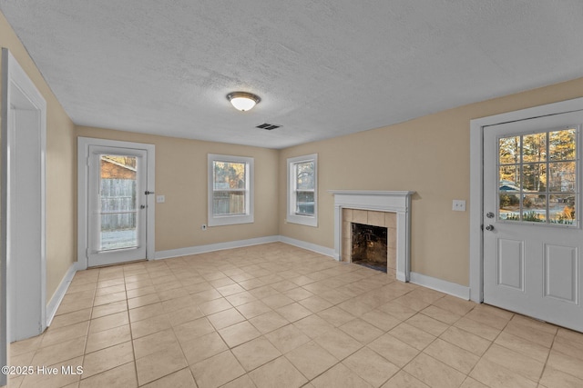 unfurnished living room with a tiled fireplace, a wealth of natural light, light tile patterned floors, and a textured ceiling