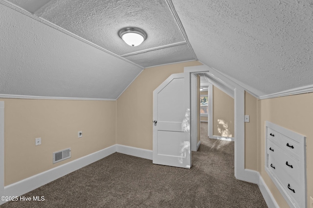 additional living space with a textured ceiling, dark carpet, and vaulted ceiling