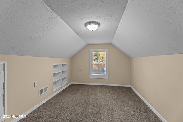 bonus room with built in shelves, lofted ceiling, carpet, and a textured ceiling