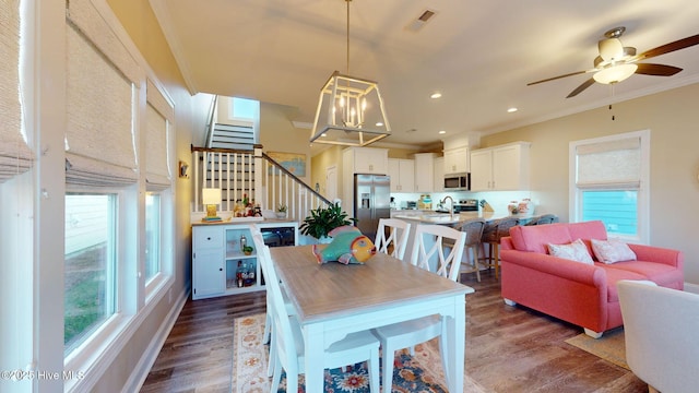 dining area featuring ornamental molding, ceiling fan with notable chandelier, dark wood-type flooring, and sink