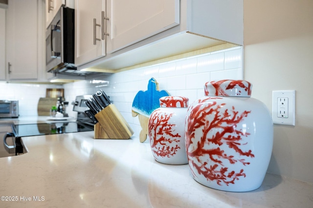 room details featuring backsplash, white cabinets, and stainless steel appliances