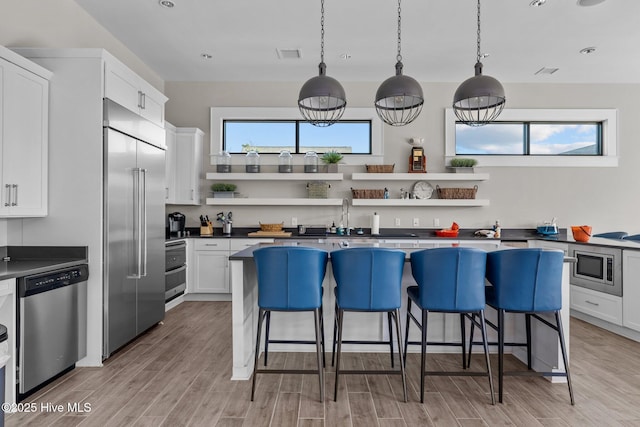 kitchen featuring a kitchen breakfast bar, built in appliances, white cabinets, and decorative light fixtures