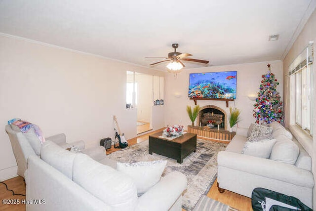 living room featuring ceiling fan, hardwood / wood-style floors, ornamental molding, and a brick fireplace