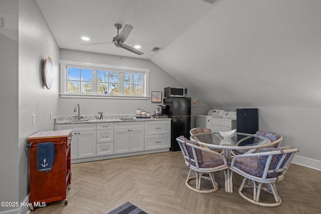 kitchen featuring lofted ceiling, black fridge, ceiling fan, separate washer and dryer, and white cabinetry