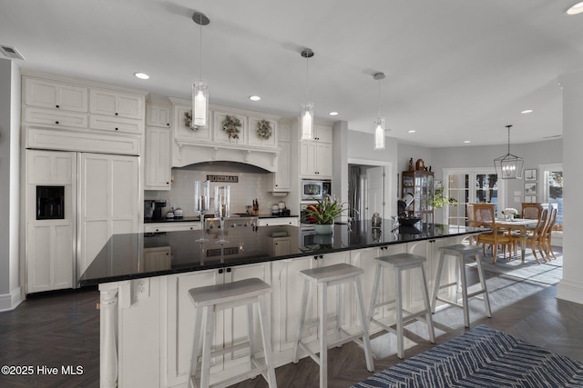 kitchen featuring dark parquet flooring, a large island with sink, hanging light fixtures, built in appliances, and a breakfast bar area