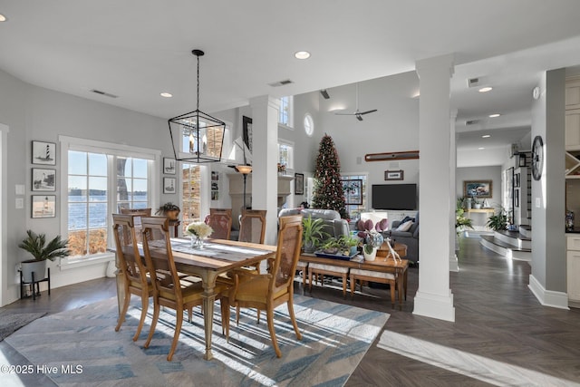 dining area with ceiling fan with notable chandelier, dark parquet floors, a water view, and decorative columns