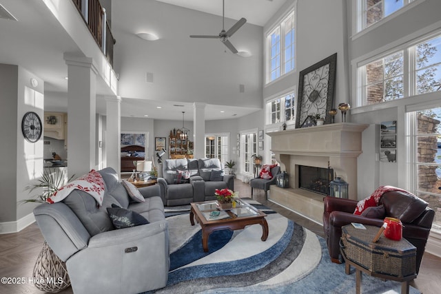 living room with ceiling fan with notable chandelier, parquet floors, a high ceiling, and a tiled fireplace