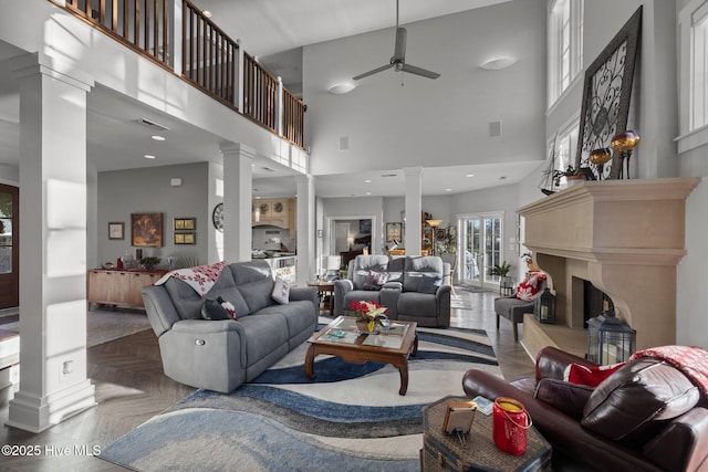 living room featuring decorative columns, parquet floors, ceiling fan, and a towering ceiling