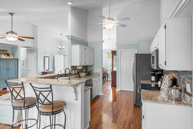 kitchen with light stone countertops, appliances with stainless steel finishes, decorative backsplash, kitchen peninsula, and a breakfast bar